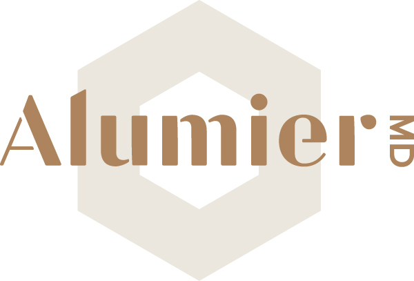 The image is a logo for Alumier MD, featuring the text "Alumier MD" in a minimalist, modern font in a brownish tone. The text is overlaid on a light, semi-transparent hexagonal shape, creating a clean and professional look that reflects exceptional aesthetics and beauty in visual design.